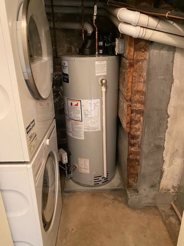 Newly installed gas water heater beside a stacked washer and dryer